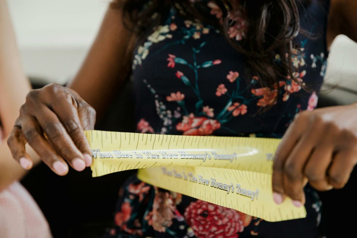 Expectant mother measuring baby bump with a floral dress and measuring tape. Perfect image for pregnancy themes.